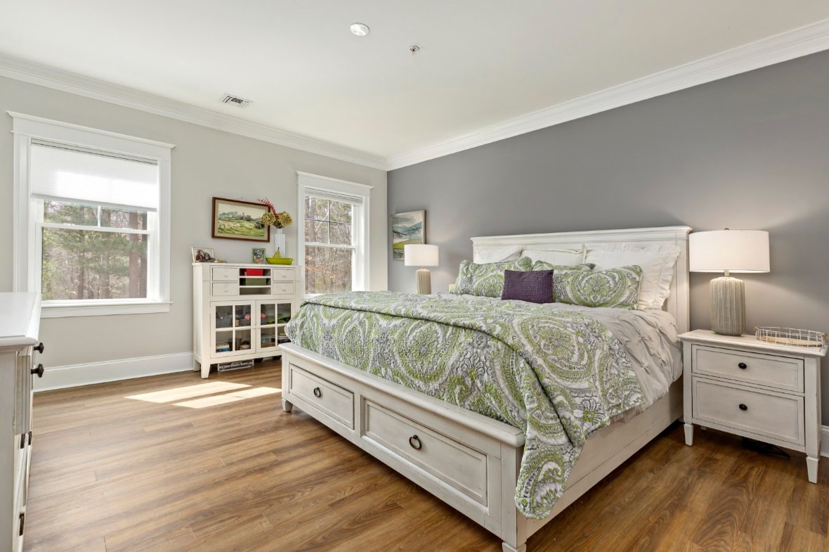 Primary bedroom with hardwood floors, gray accent wall, and wooded views