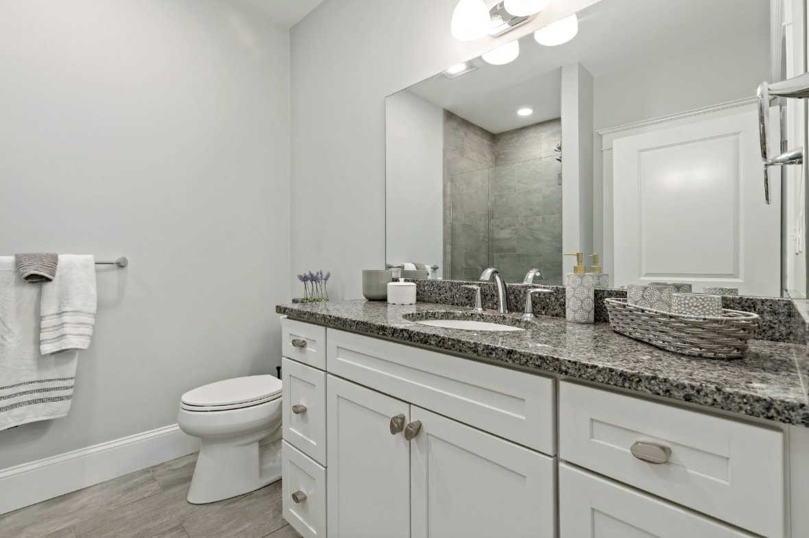 Primary bath with granite countertop, white cabinetry, and tile shower